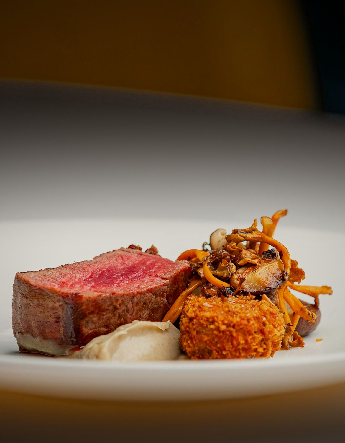Seared Angus fillet with wild mushrooms, a potato croquette and celeriac purée on a white plate